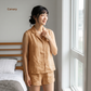 Woman wearing a beige linen set standing by a window in a bedroom.