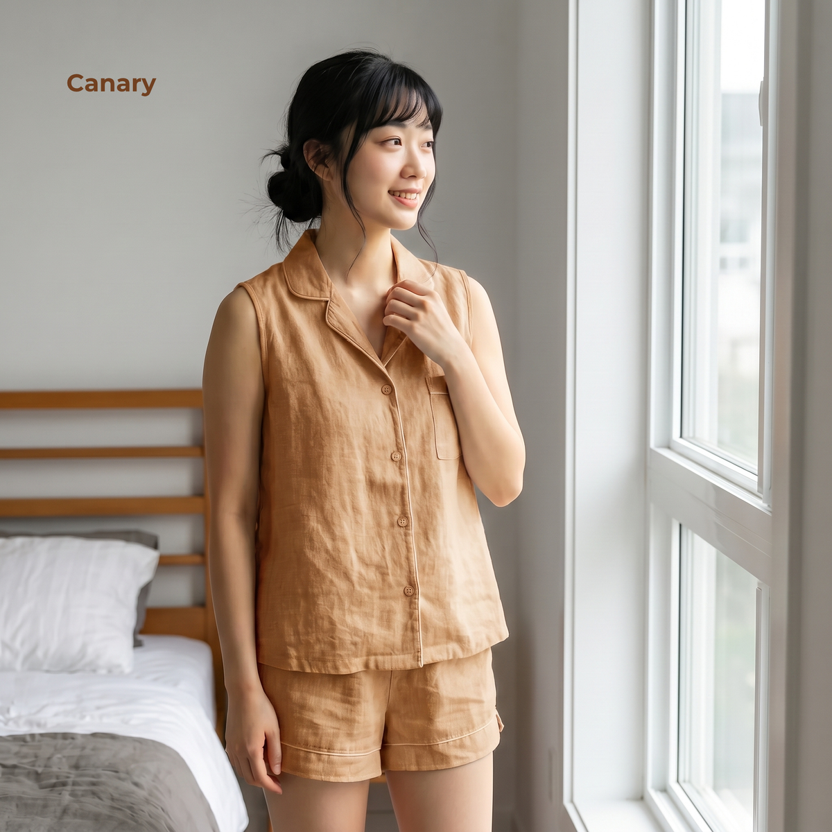 Woman wearing a beige linen set standing by a window in a bedroom.