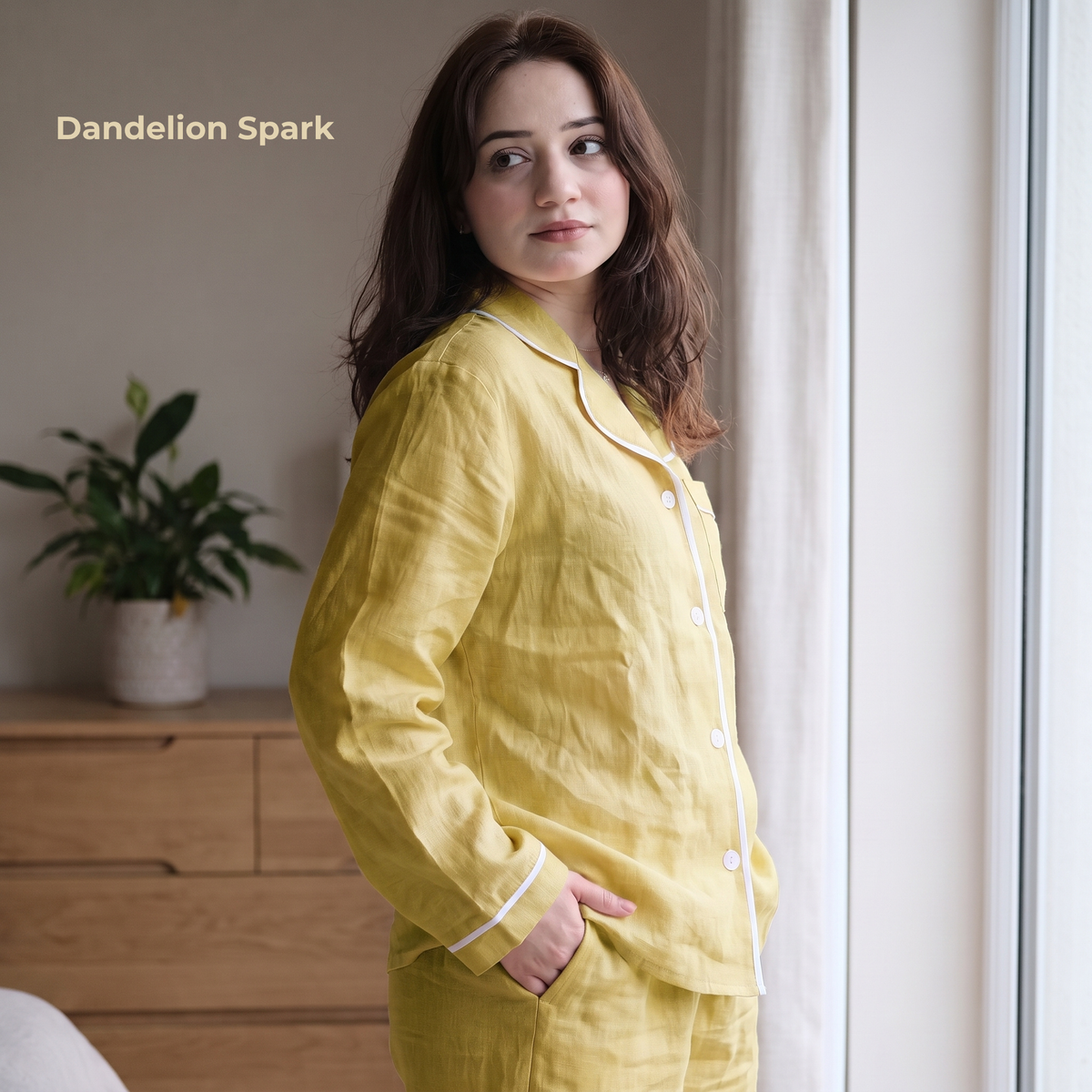 Woman wearing yellow pajamas standing in a room with a plant and wooden dresser.