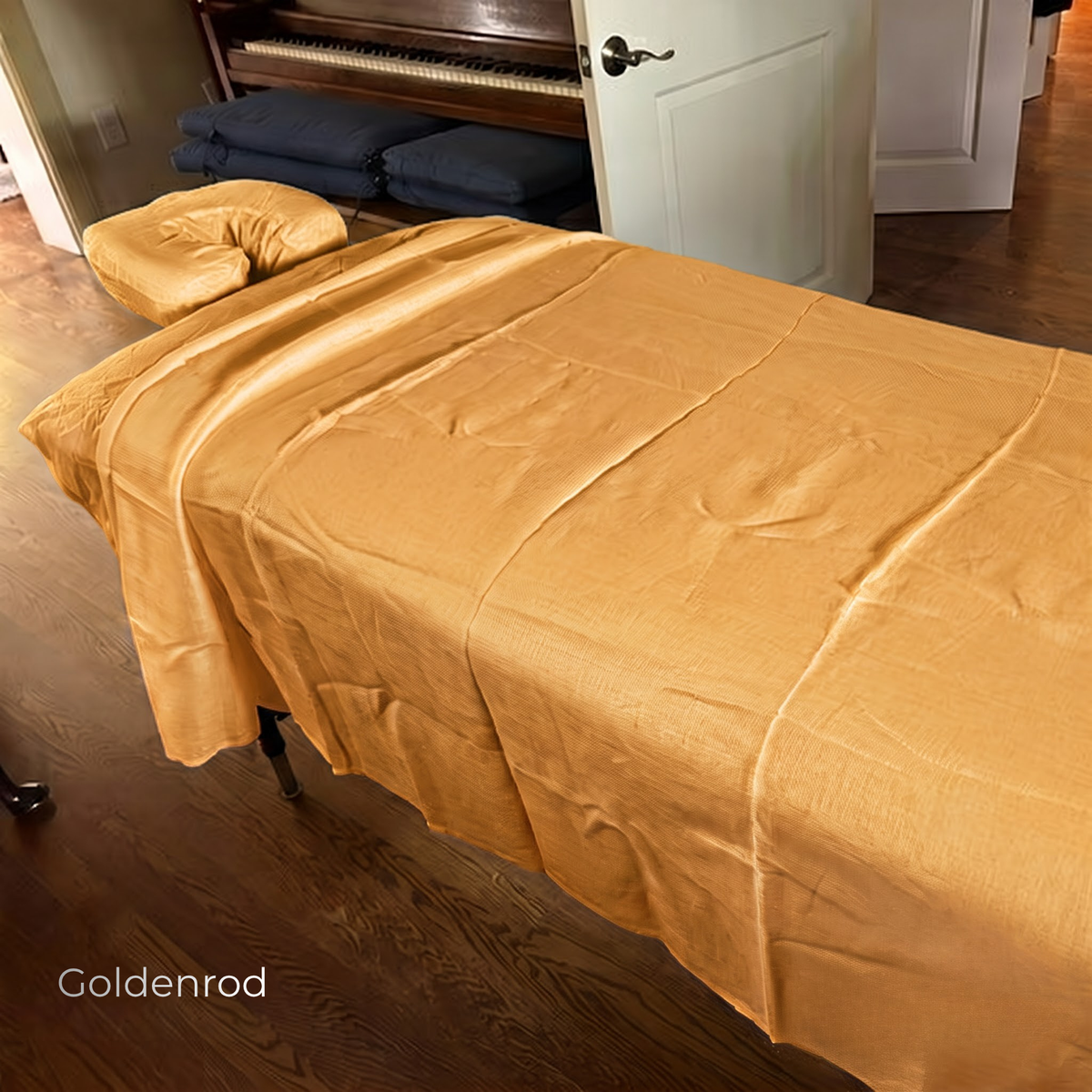 A goldenrod satin sheet draped over a massage table in a room with dark wood floors and a piano in the background. The text 'Goldenrod' is visible in the bottom-left corner.