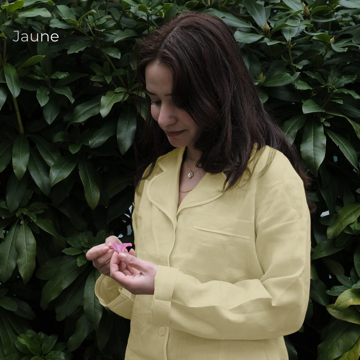 Woman in a yellow shirt holding a pink object against a green leafy background