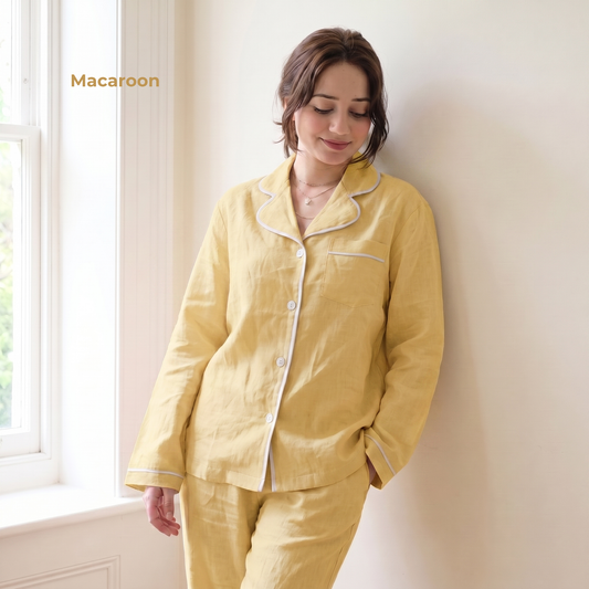 Woman wearing yellow pajamas leaning against a wall with a window in the background.