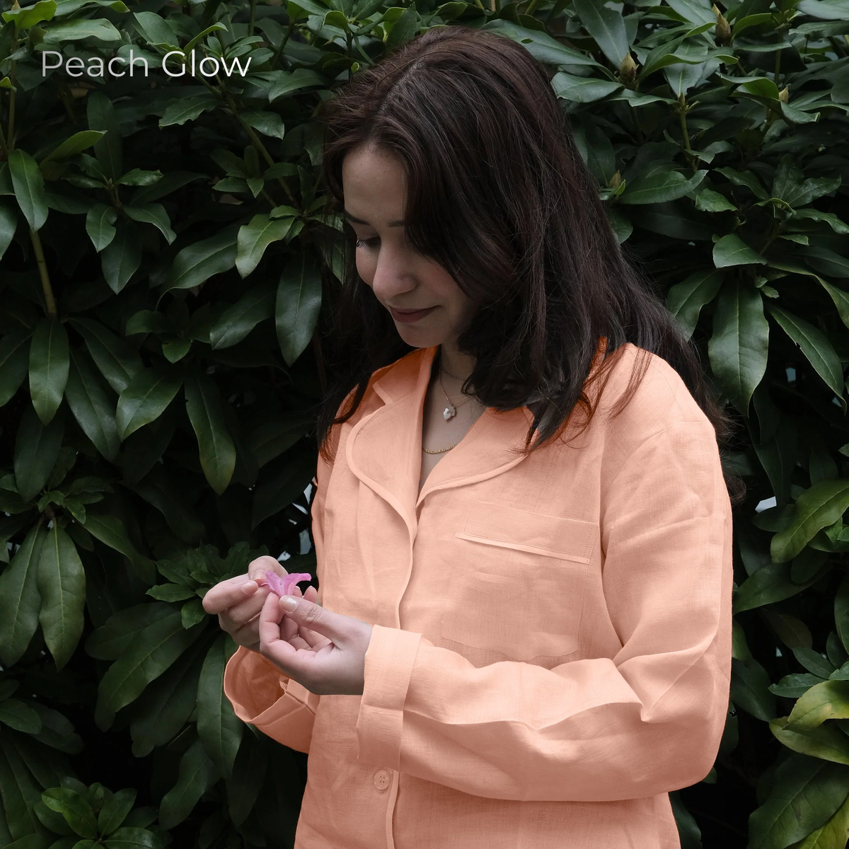 Woman in peach shirt holding a pink flower against a green leafy background