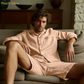 Man wearing a peach-colored lounge set sitting on a couch in a cozy room.