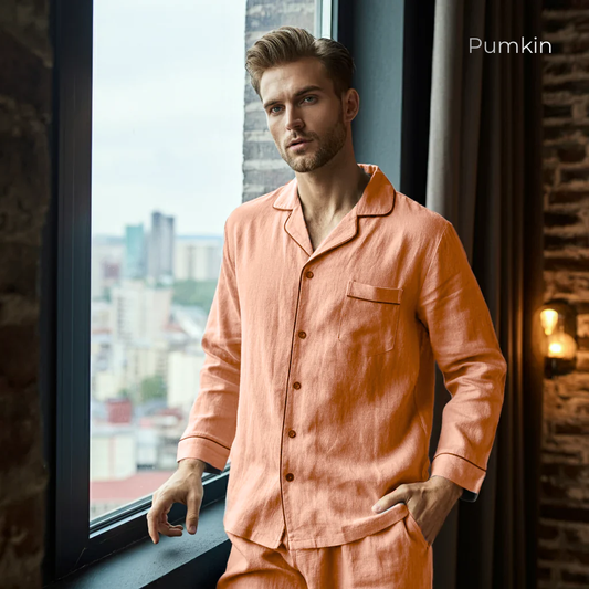 Man wearing peach-colored pajamas standing by a window with a cityscape view.
