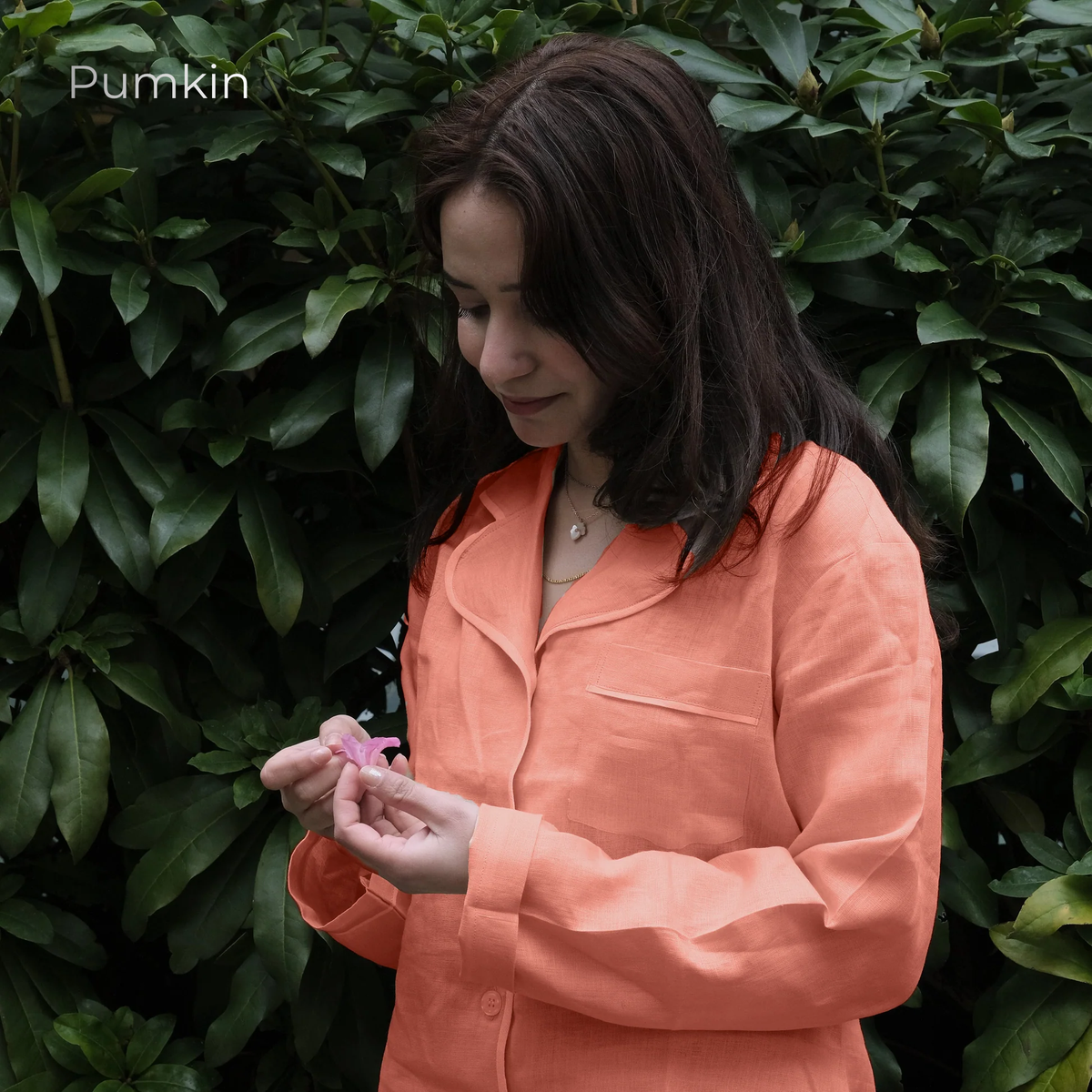 Woman in an orange shirt holding a pink flower against a green leafy background