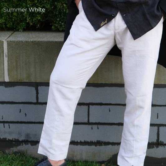 A person wearing white linen trousers and a black shirt, standing outdoors against a gray brick wall.