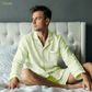 Man wearing light green pajamas sitting on a bed with a neutral background