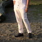 A person outdoors wearing light beige linen trousers, a white short-sleeve button-up shirt, and black shoes, standing on sandy ground with a log in the background.