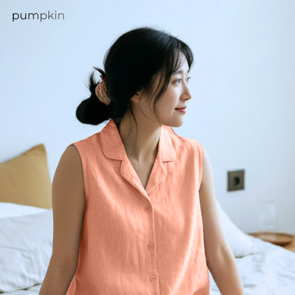 Woman wearing a peach-colored sleeveless shirt sitting on a bed with a blurred background